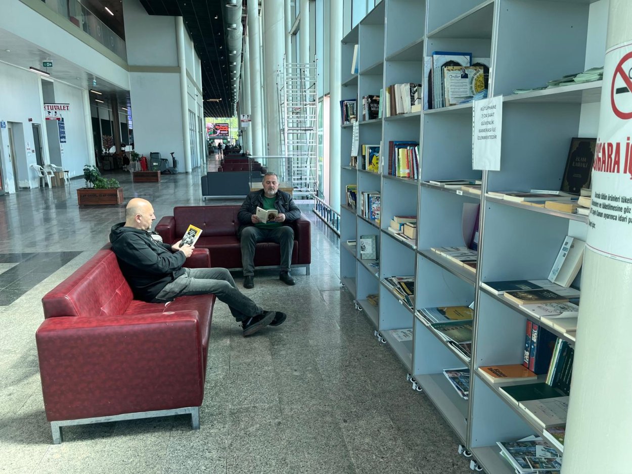 YOLCULAR OTOBÜSLERİNİ KİTAP OKUYARAK BEKLİYOR